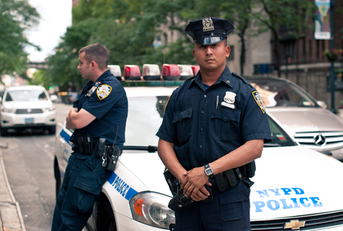 shutterstock_109593020.jpg Two NYPD officers standing near a police car in an urban environment