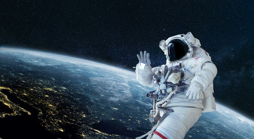 shutterstock_1936566580.jpg Astronaut floating in space above Earth, waving.