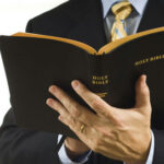 Evangelist MURDERED After Muslim Conversions—Where’s Outrage? Man in suit holding an open Holy Bible.