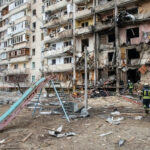 Kyiv’s Night TERROR: Missile Onslaught Unleashed! Damaged apartment building with debris scattered firefighters present.