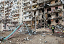 Kyiv’s Night TERROR: Missile Onslaught Unleashed! Damaged apartment building with debris scattered firefighters present.