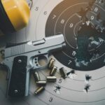 A handgun placed on a shooting target with bullet holes and spent cartridges nearby