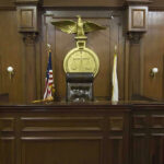 The Charlie Kirk Case Just Took A Stunning Turn Judges bench in an empty courtroom, scales emblem above.