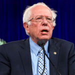 Sanders’ AI Grab Sparks Market Panic Bernie Sanders speaking at an event, wearing a suit.