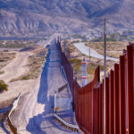Border Brawl Explodes on Tribal Land Border wall stretching through desert landscape with mountains.