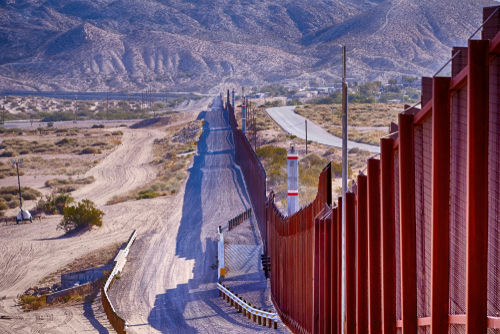 shutterstock_1552272005 Border wall stretching through desert landscape with mountains.