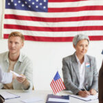 Most Expensive Primary Ever — Lesson Delivered Election workers assist voters at a registration table with a U.S. flag behind them