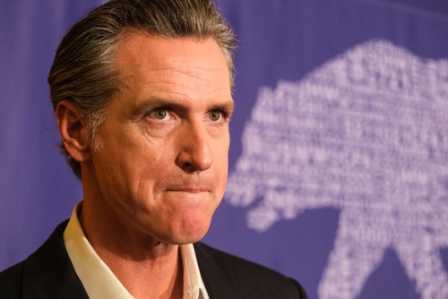 Gov.,Gavin,Newsom,Signs,The,Fast,Food,Bill,Ab1228,In A serious-looking political figure at a press event with a bear graphic in the background