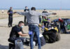 Police officers assist migrants on a beach.