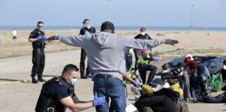Police officers assist migrants on a beach.
