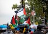 Crowd at a rainy street protest with Palestinian flags and umbrellas