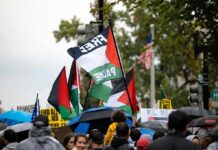 Cuba-Linked Protest Plan Targets U.S. Bases Crowd at a rainy street protest with Palestinian flags and umbrellas