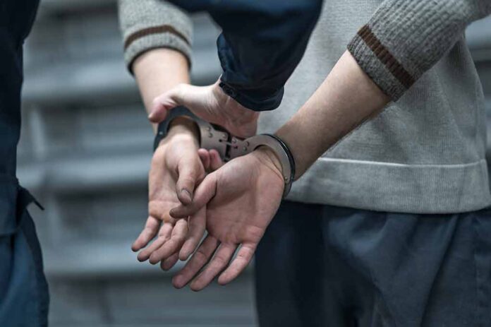 Person in handcuffs being detained by another person.