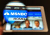 Magnifying glass over tablet displaying MSNBC homepage.