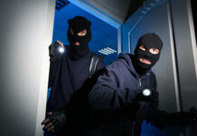 Two masked individuals in dark clothing breaking in.