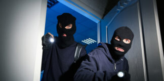 Two masked individuals in dark clothing breaking in.