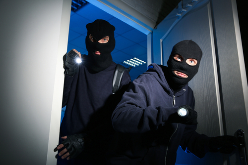 Two masked individuals in dark clothing breaking in.