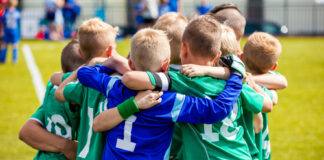 Children in sports uniforms huddling on a soccer field.