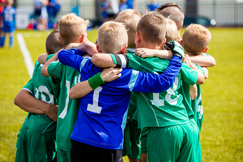 Children in sports uniforms huddling on a soccer field.