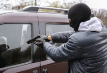 Masked person pointing gun at vehicles window.